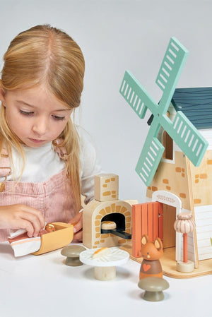 A young girl plays with the Tender Leaf Wooden Toys Penny Windmill set, featuring a colorful wooden windmill, cozy house, and charming animal figures, promoting imaginative and eco-friendly play.