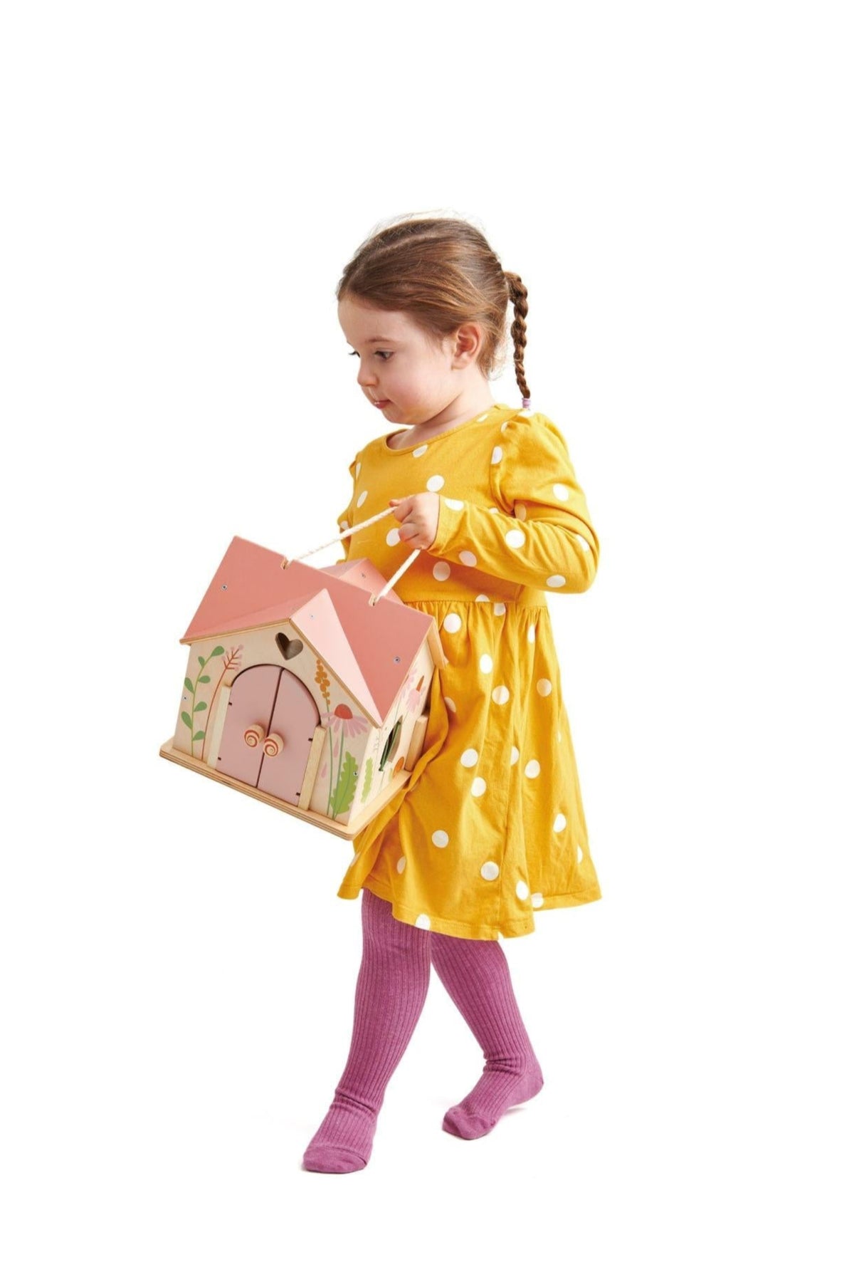 A young girl in a yellow polka dot dress carries the Tender Leaf Wooden Toys Rosewood Cottage, showcasing its charming.