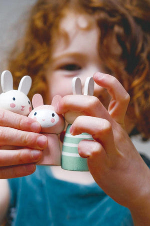 A child with curly red hair holds three colorful wooden bunny figures, showcasing their playful design and cheerful expressions.