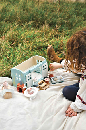 A child interacts with the Tender Leaf Wooden Toys shepherds hut set on a grassy surface, featuring colorful wooden animals and accessories, promoting imaginative play and eco-friendly design.