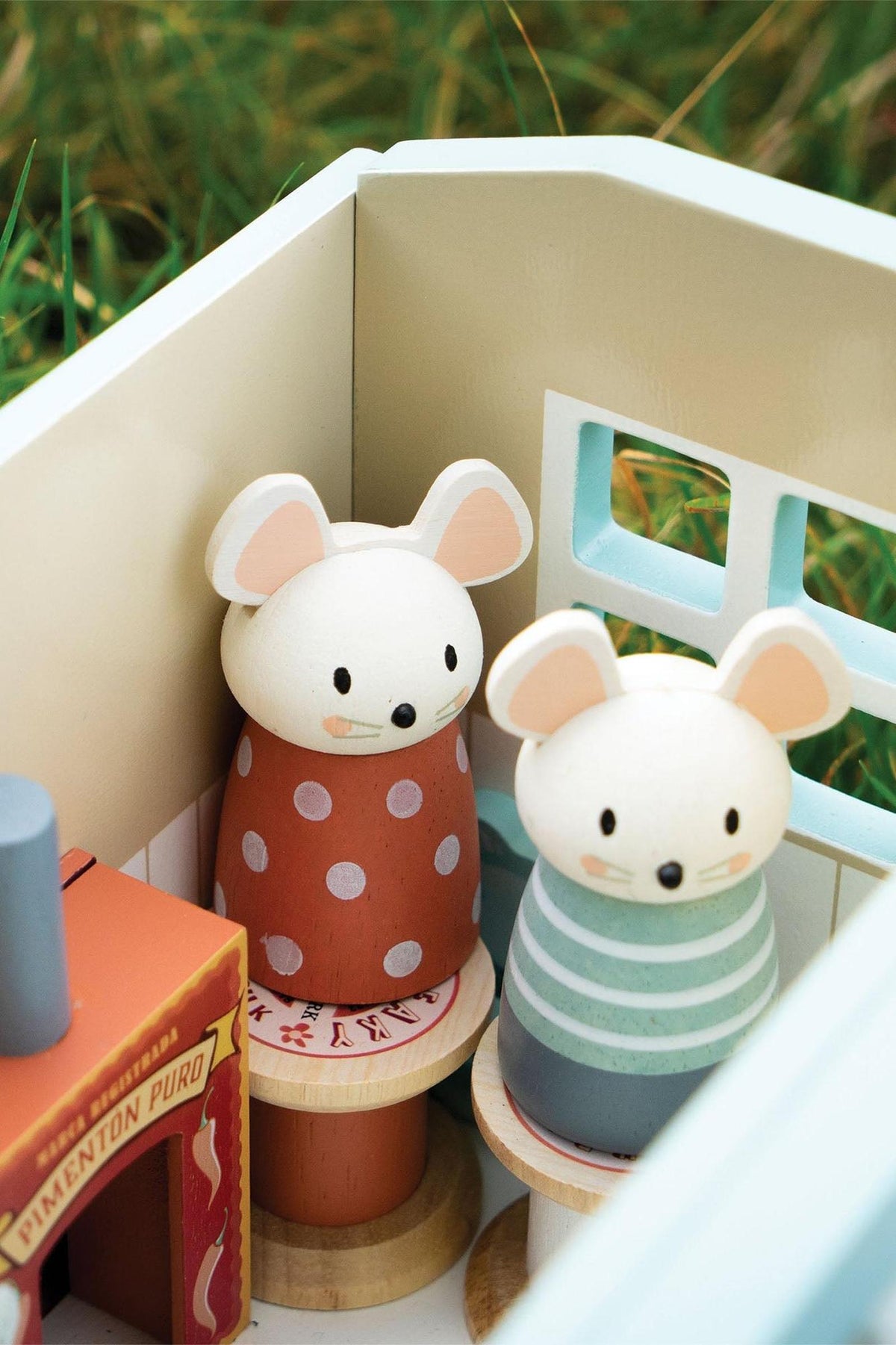 Two charming wooden mice figurines with distinct patterns stand inside a brightly colored shepherds hut. The hut features soft pastel colors and a cozy, imaginative design for creative play.