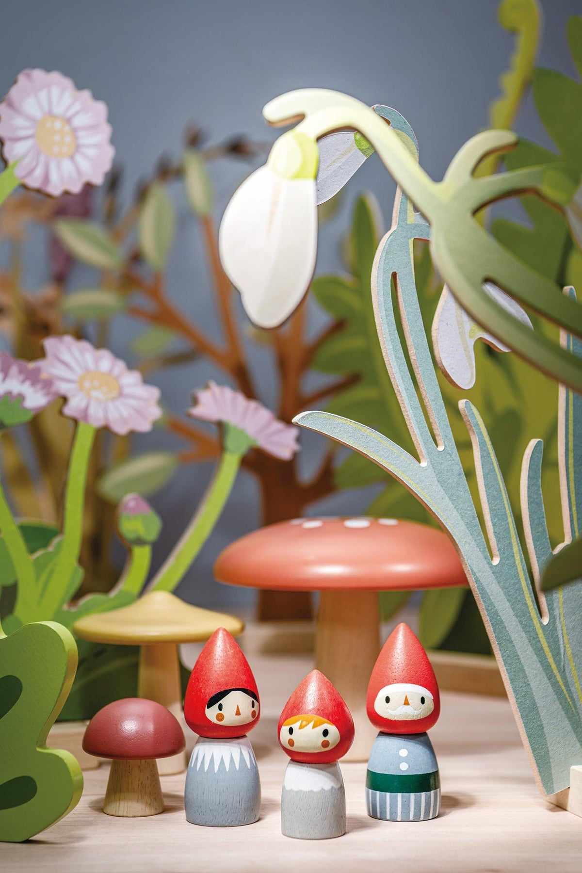 A charming wooden gnome family stands among colorful toadstools and greenery, featuring vibrant red hats and hand-painted details. This sustainable, eco-friendly toy encourages imaginative play for young children.