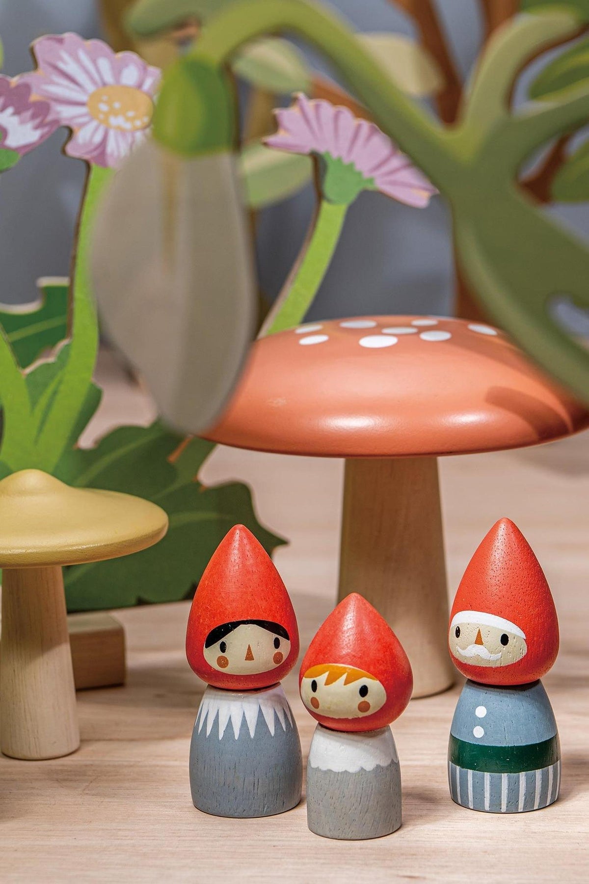 A charming set of wooden gnome figurines, crafted from sustainable materials, features two gnomes with red hats and painted faces, surrounded by colorful toadstools and vibrant floral elements.