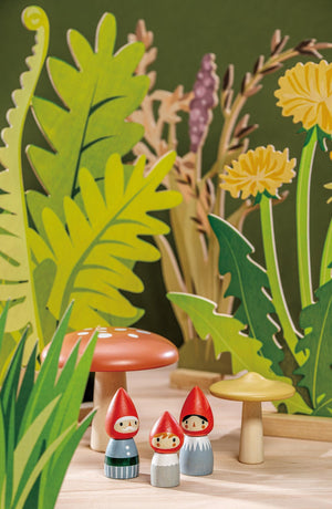 A colorful wooden scene featuring a gnome family with red hoods, surrounded by vibrant greenery, mushrooms, and flowers. This eco-friendly set encourages imaginative play for young children.