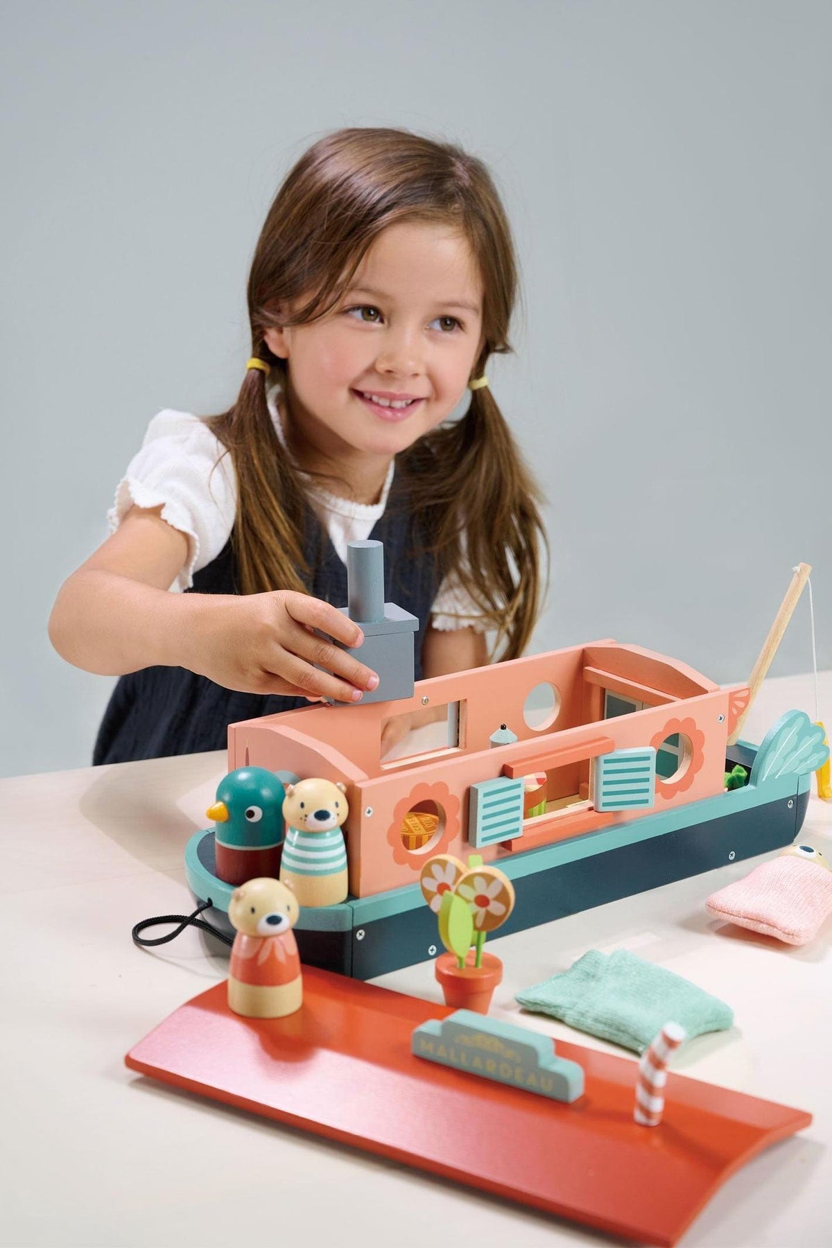 A young girl smiles while playing with the Tender Leaf Wooden Toys Little Otter Canal Boat, featuring colorful wooden figures and accessories, designed for imaginative play and eco-friendly fun.