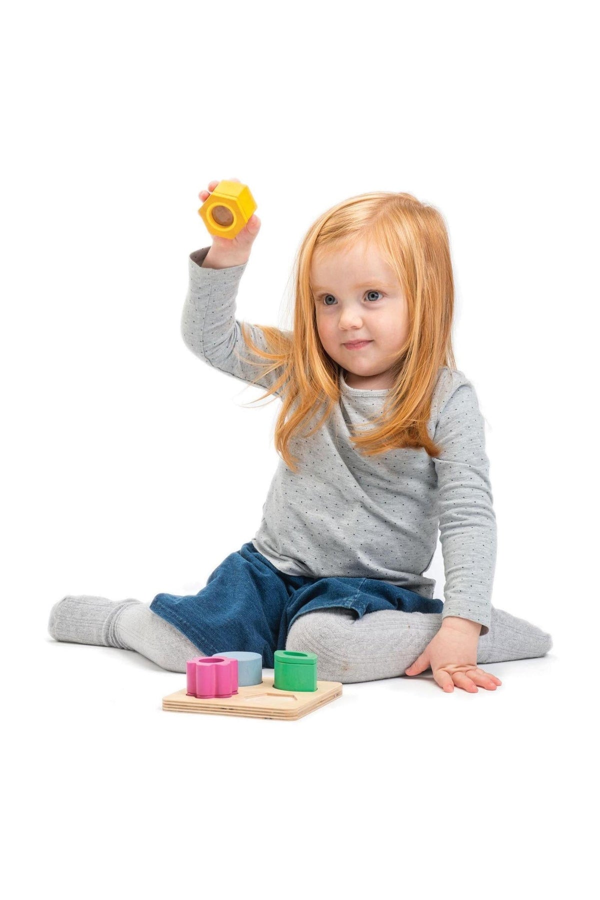 A young child with red hair plays with colorful wooden blocks on a white background, wearing a gray outfit.