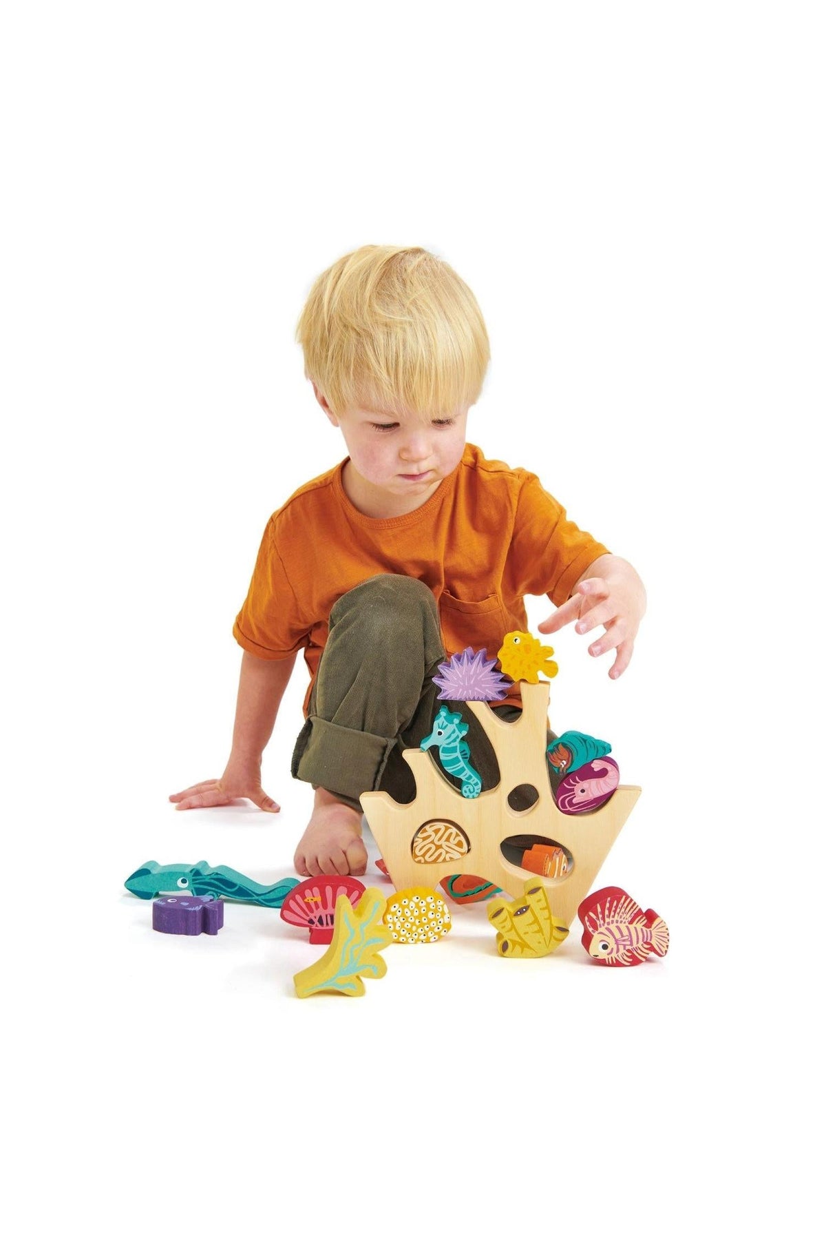 A child with blonde hair plays with a colorful wooden coral reef stacking toy featuring various sea creatures.