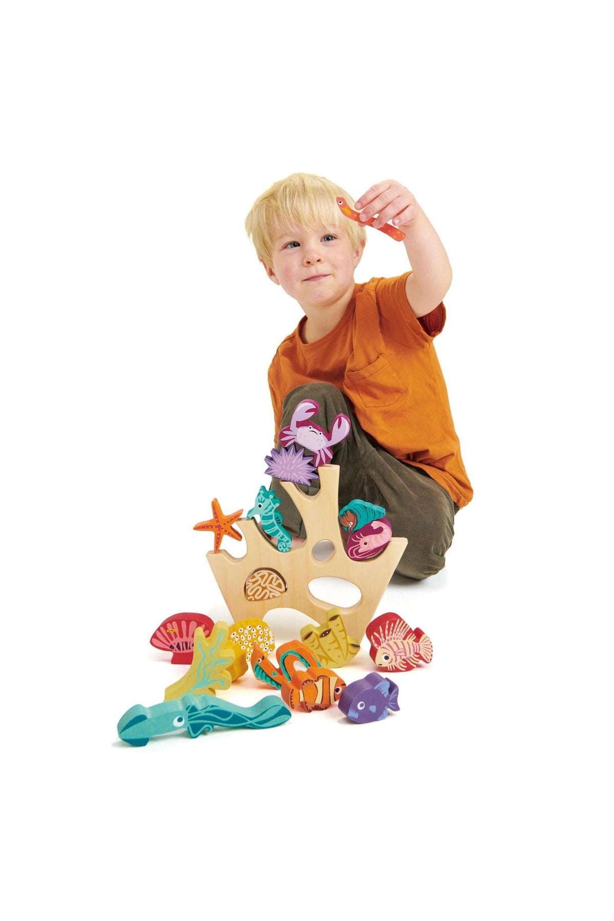 A young child holds a colorful wooden sea creature while surrounded by various brightly painted marine life and a coral.