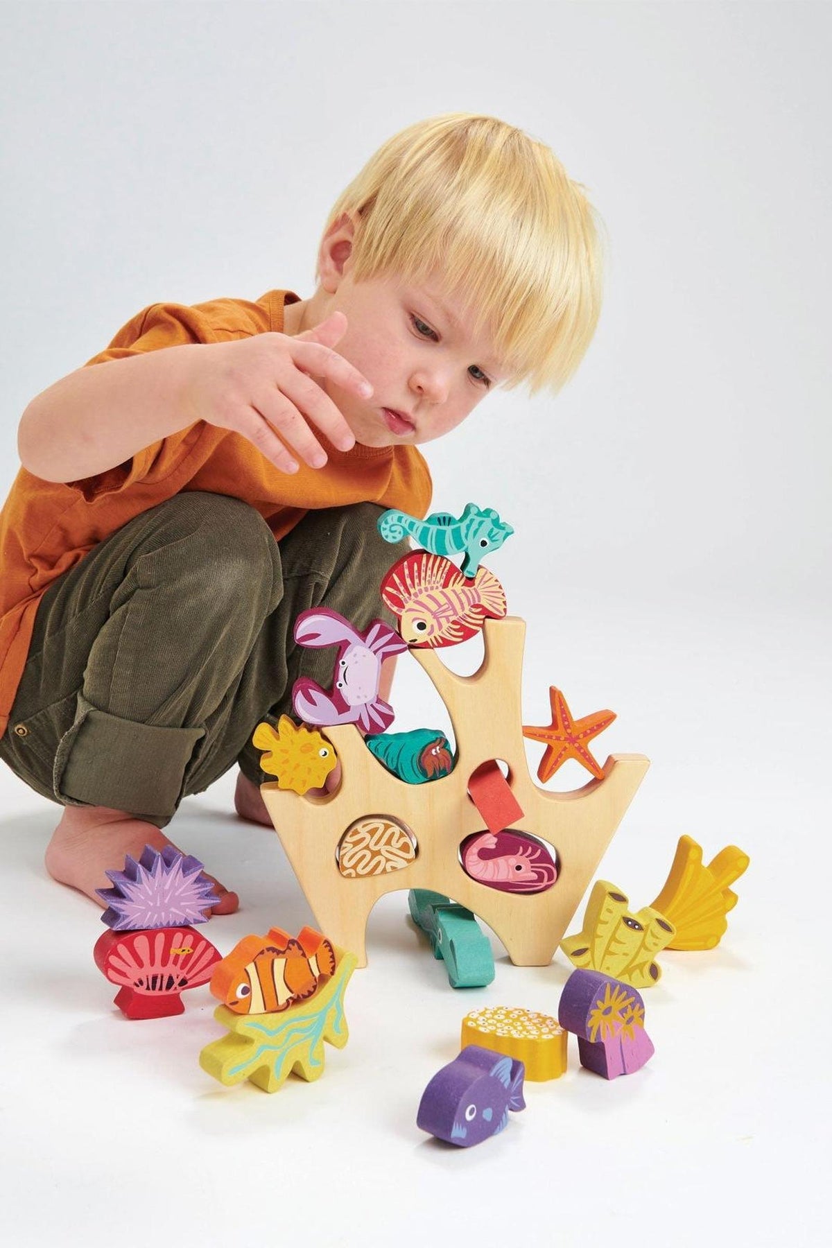 A child plays with a colorful wooden stacking coral reef toy featuring various sea creatures and a natural wood base.