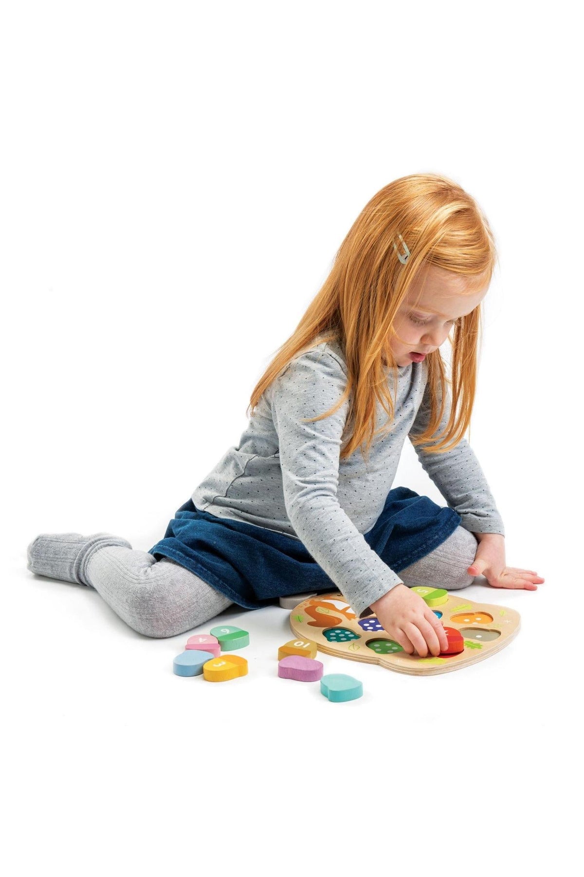 A young child with red hair sits on the floor, focused on a wooden shape-sorting toy featuring colorful pieces.