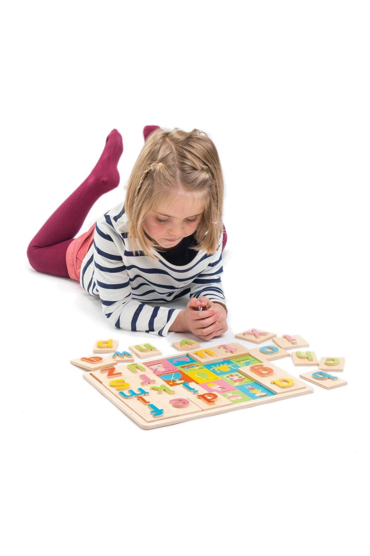 A young girl lies on her stomach, playing with a colorful wooden alphabet puzzle. The toy features vibrant letters and corresponding images, promoting language development in children aged 18 months.