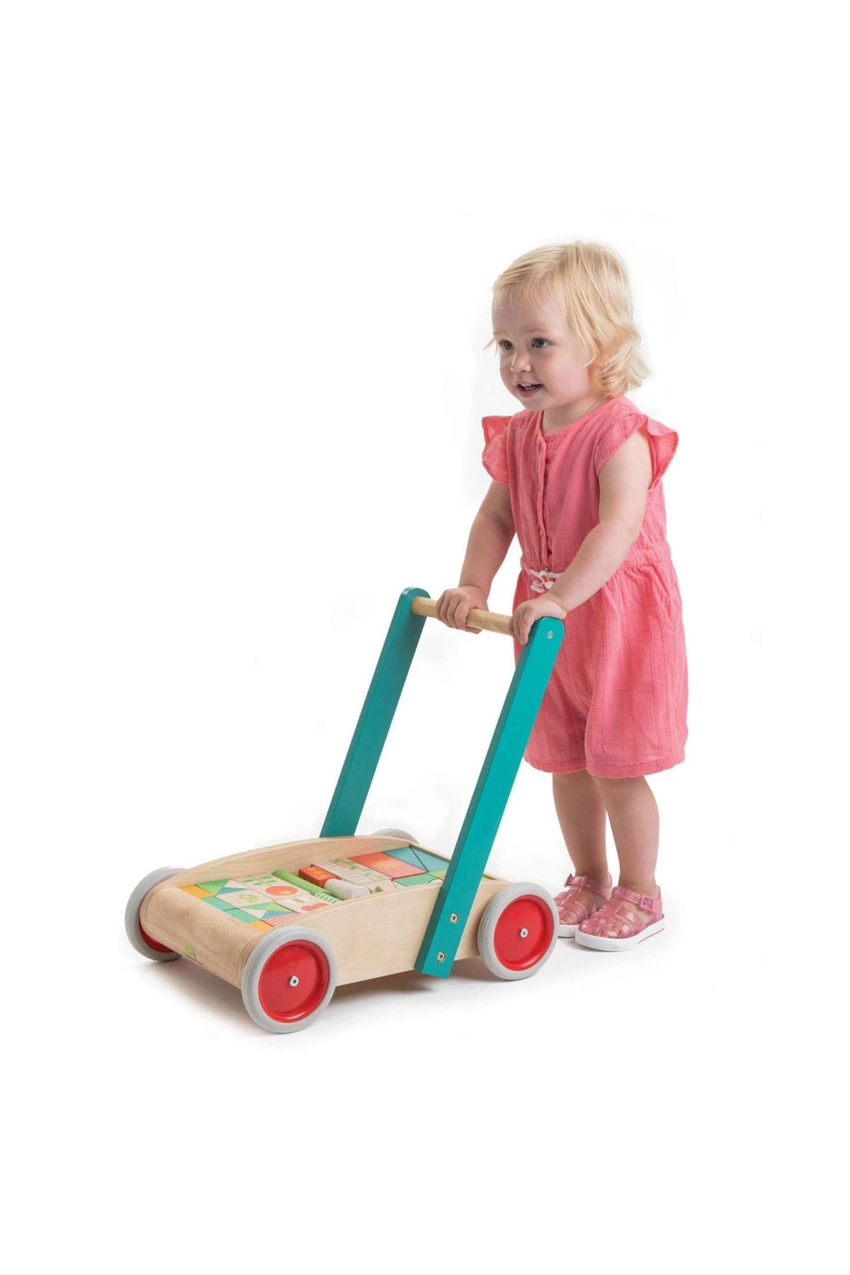 A young child in a pink dress smiles while pushing a colorful wooden baby block walker with sturdy teal handles and red wheels, promoting safe and imaginative play.
