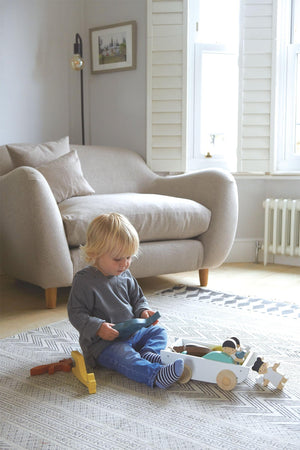 A child sits on a textured rug, playing with a wooden toy in a cozy, well-lit living room.
