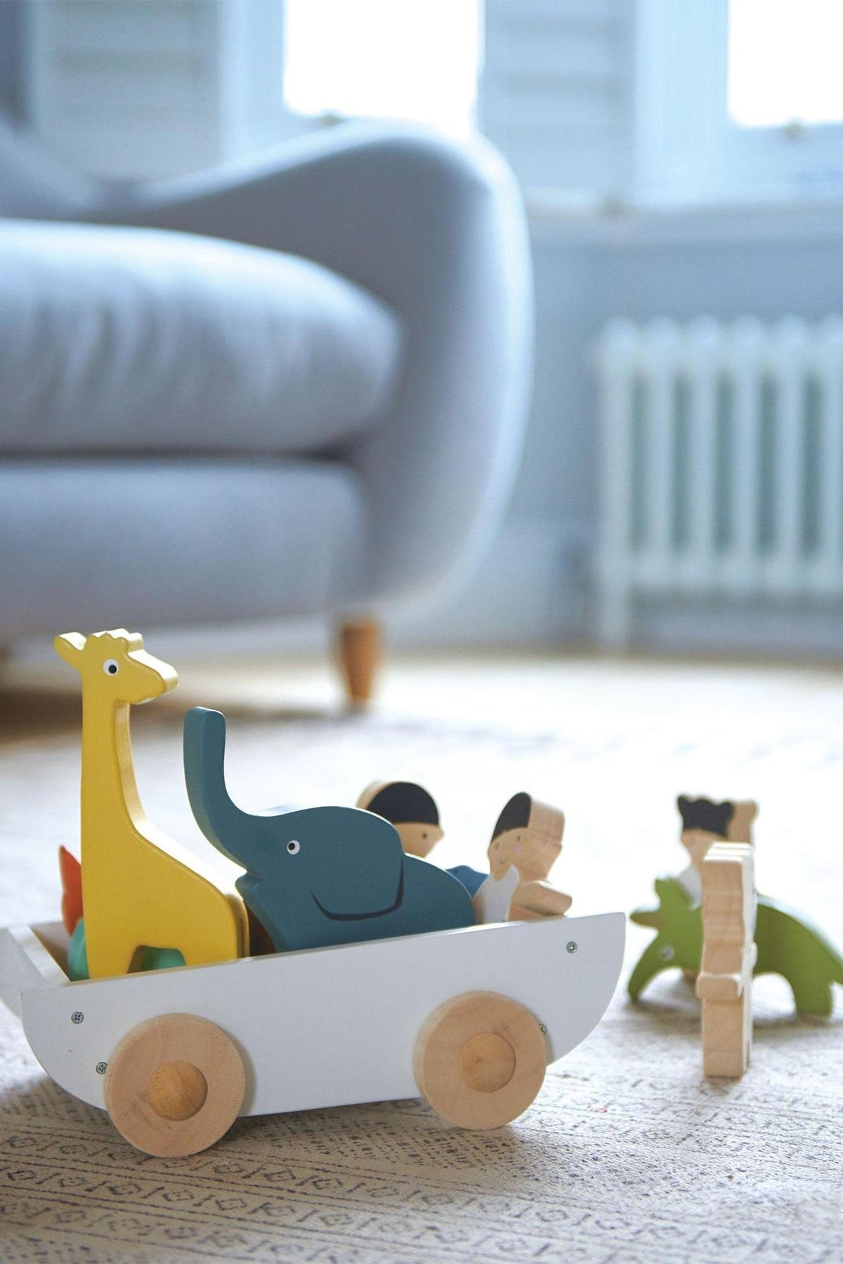 Colorful wooden toy boat featuring a giraffe, elephant, and two children, crafted from sustainable materials, set on a light rug.