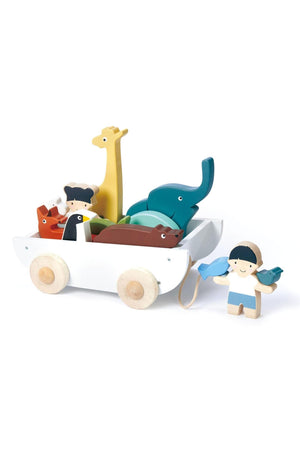 A wooden toy boat carries colorful animal figures, including an elephant and giraffe, alongside a boy holding a bird.