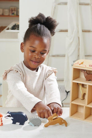 A young girl with curly hair is playing with colorful wooden animal figures on a light-colored table.