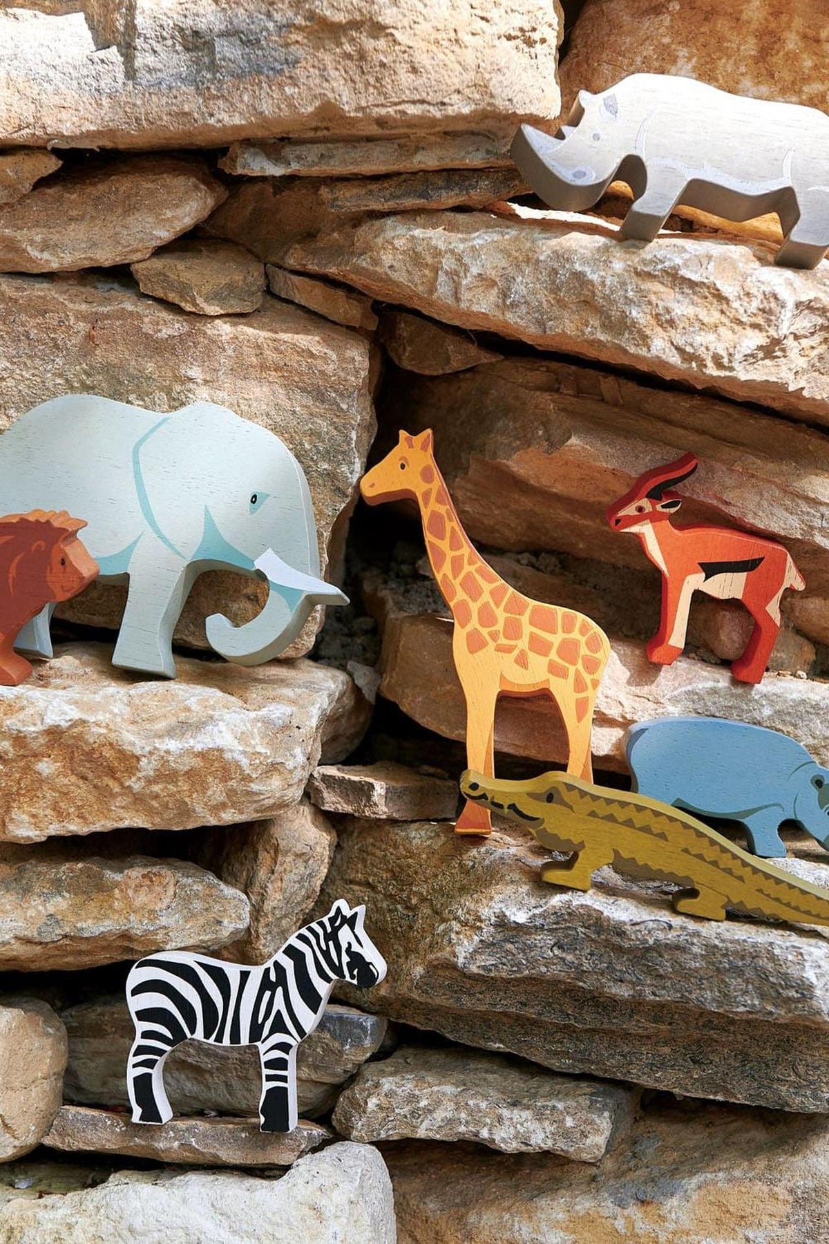 Colorful wooden animal figures, including an elephant, giraffe, and lion, are displayed on a stone backdrop, showcasing the Tender Leaf.
