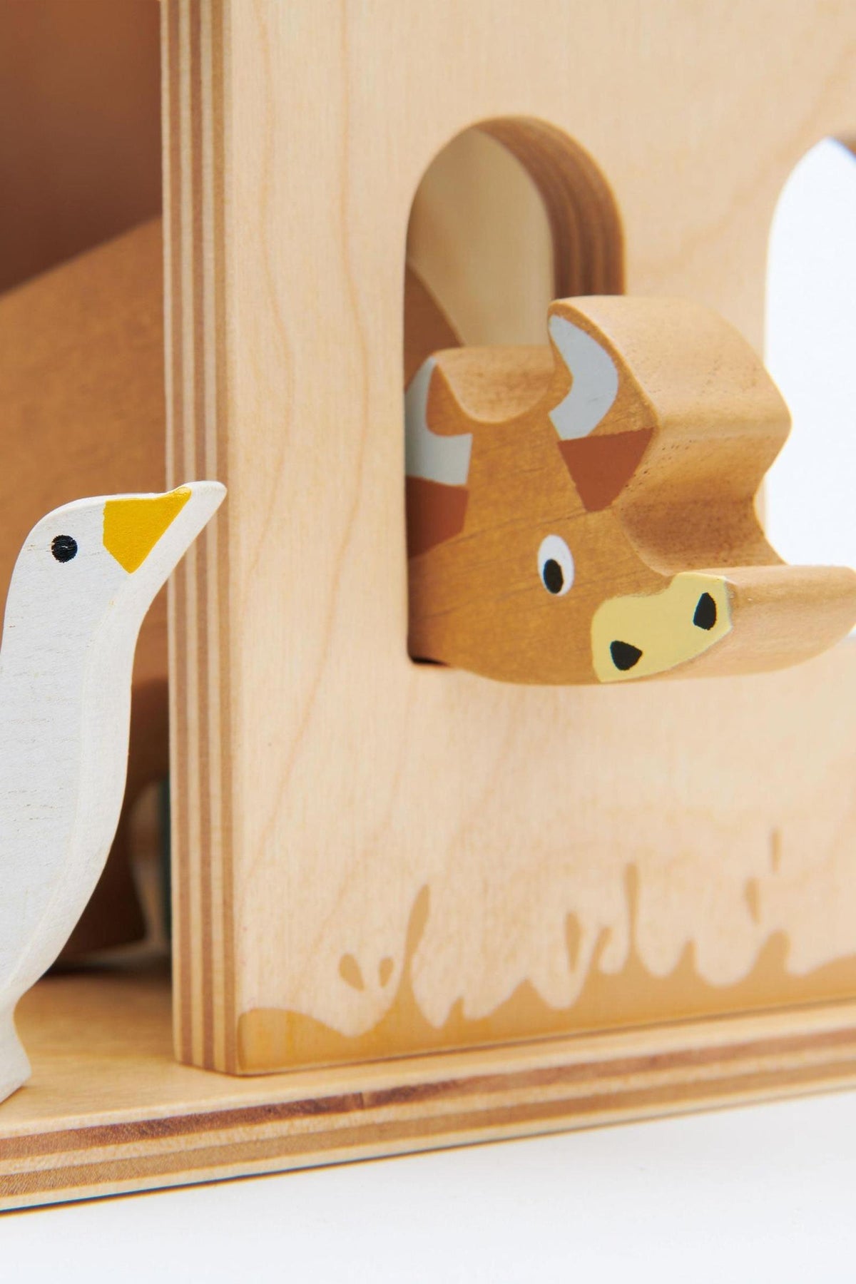 A wooden farm toy featuring a cow peeking through a barn window and a white goose nearby, crafted from sustainable.