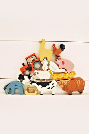A colorful assortment of wooden farmyard animals, including a cow, sheep, and pig, is stacked alongside a red tractor.