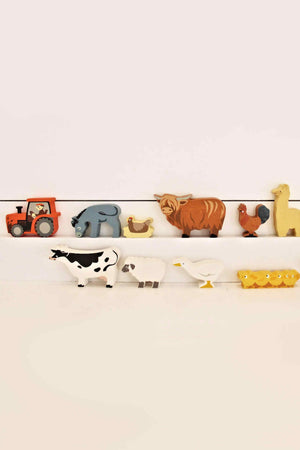 A display of Tender Leaf Wooden Toys features colorful farmyard animals, including a tractor, cow, goose, and sheep, showcasing sustainable wooden construction. Ideal for children aged three and older.
