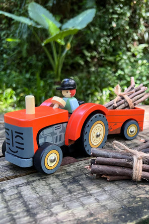 A vibrant red wooden tractor with a removable trailer carries bundled sticks, featuring a playful driver. This eco-friendly toy inspires imaginative play for young children in outdoor settings.