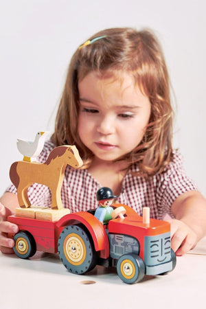 A child plays with a red wooden tractor toy, featuring a horse and a goose on top, promoting imaginative play.