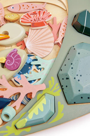 Colorful wooden pieces representing sea life, including fish, shells, and coral, are arranged around a pale green base, showcasing a sustainable and engaging design for children’s play.