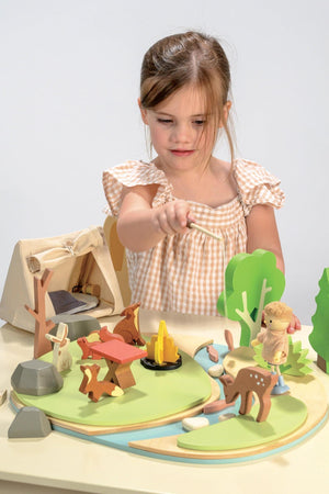 A child plays with the Tender Leaf Wooden Toys Wildlife Camping Playset, featuring wooden animals, trees, and a tent.