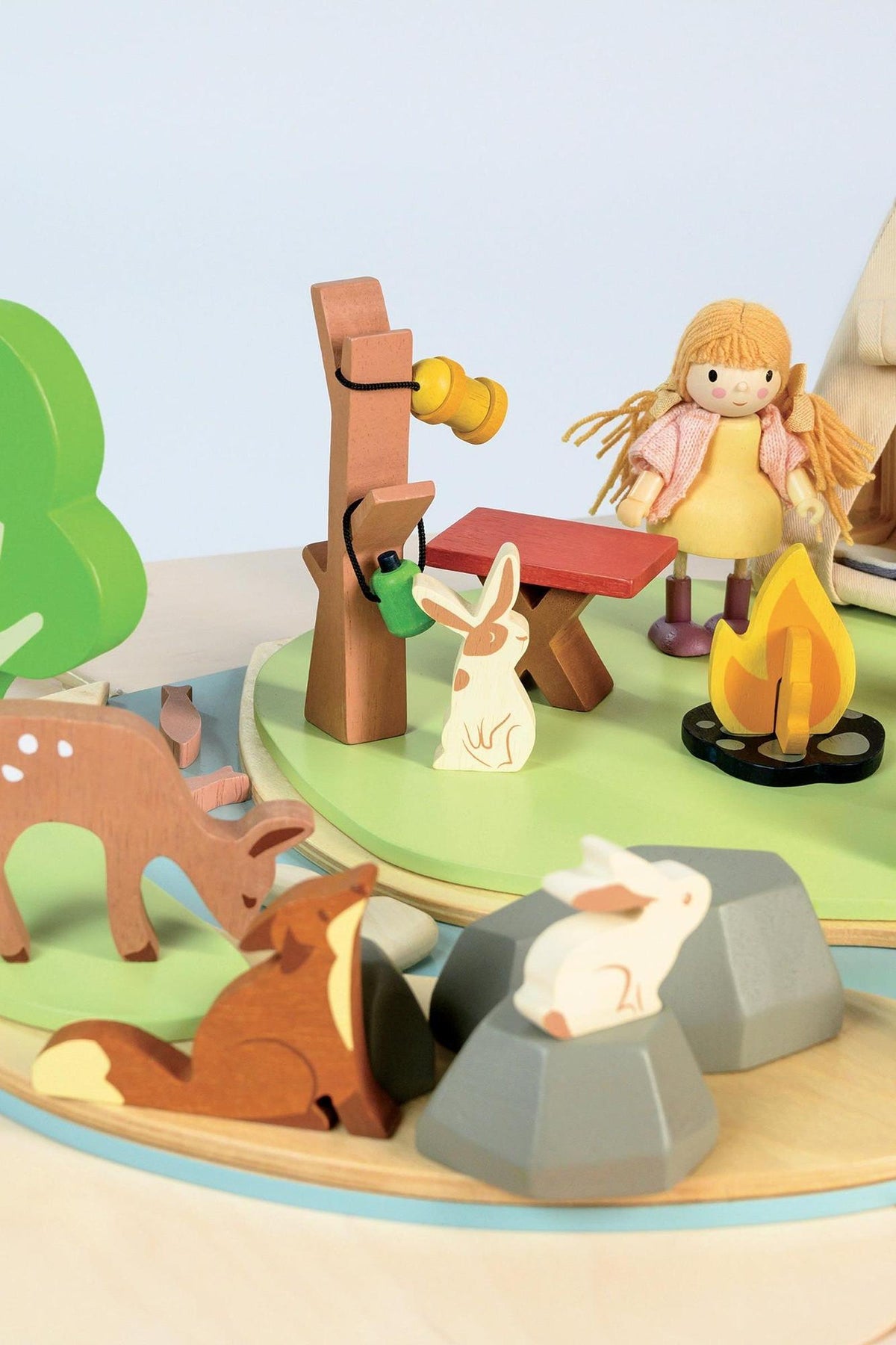 Wooden toy campsite with animals, tree, bench, and doll. Features eco-friendly materials and vibrant colors.