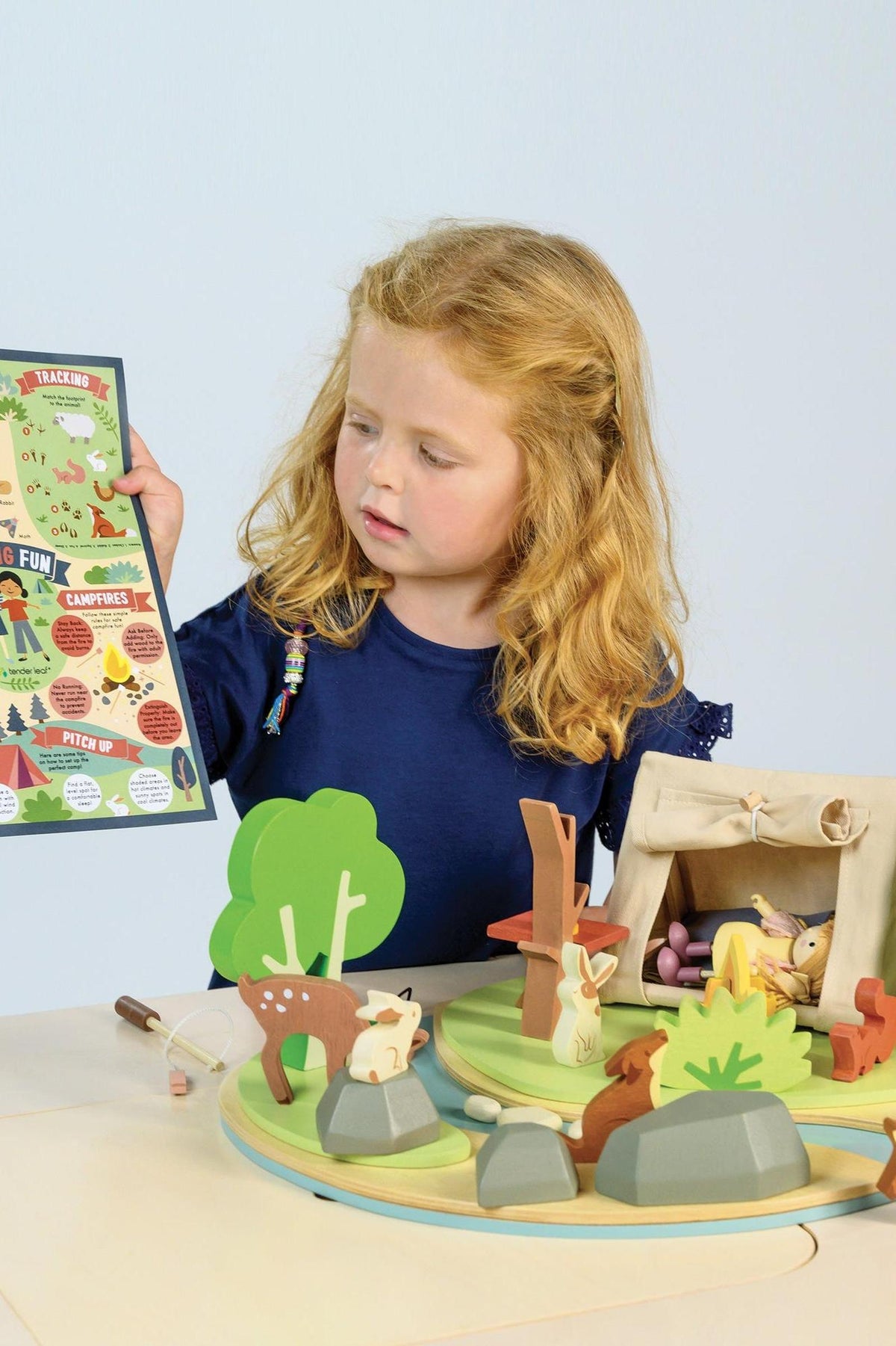 A child plays with a Tender Leaf Wooden Toys camping set featuring colorful animals, trees, and a tent.