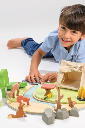 A child plays with a Tender Leaf wooden camping playset featuring a tent, wildlife figures, and accessories.