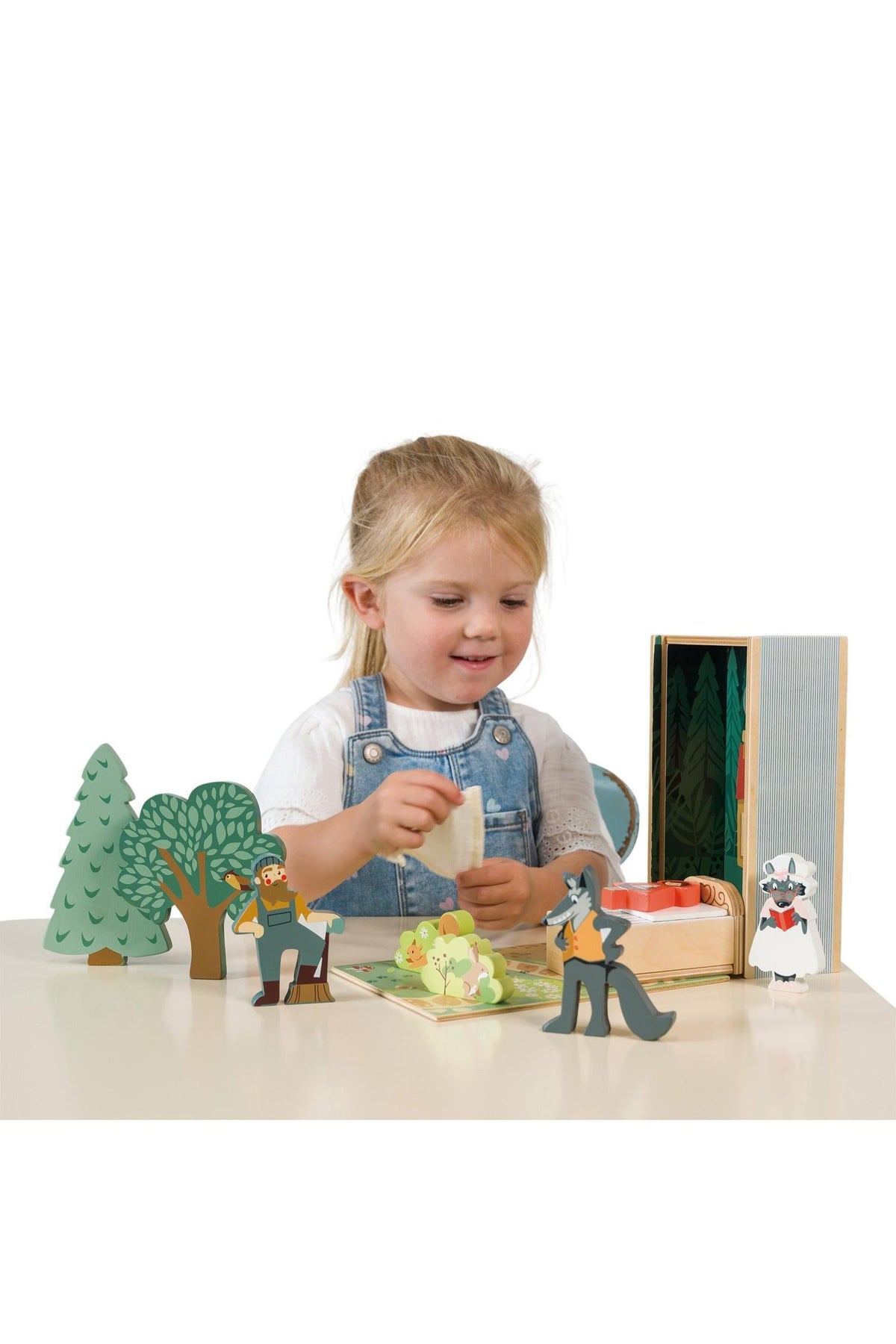 A young child interacts with a colorful wooden storytelling set featuring characters and trees from the Little Red Riding Hood tale. The eco-friendly materials promote imaginative play and creativity.