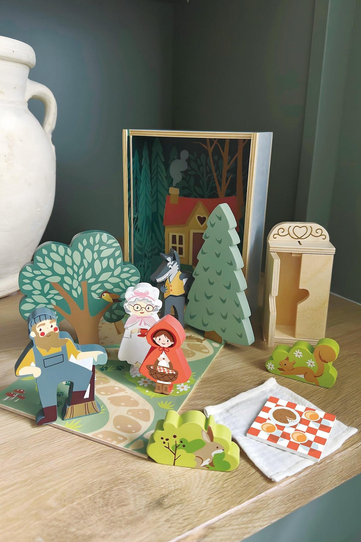 A colorful wooden storytelling set from Tender Leaf Toys features characters from Little Red Riding Hood, including a cottage scene, trees, and props, encouraging imaginative play for children.