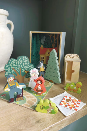 A colorful wooden storytelling set from Tender Leaf Toys features characters from Little Red Riding Hood, including a cottage scene, trees, and props, encouraging imaginative play for children.