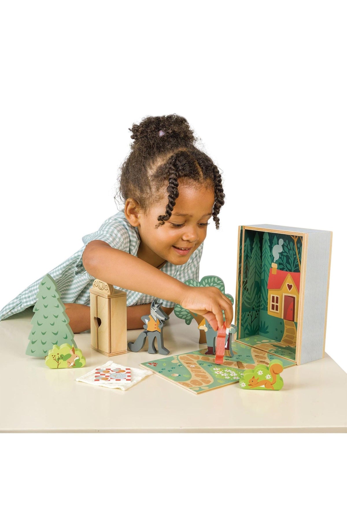 A young girl joyfully plays with the Tender Leaf Wooden Toys Little Red Riding Hood set, featuring vibrant wooden pieces, a forest scene, and a charming wooden box.