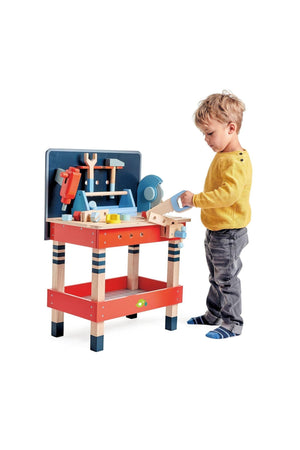 A child plays with the Tender Leaf Wooden Toys tool bench, featuring colorful wooden tools and a sturdy design.