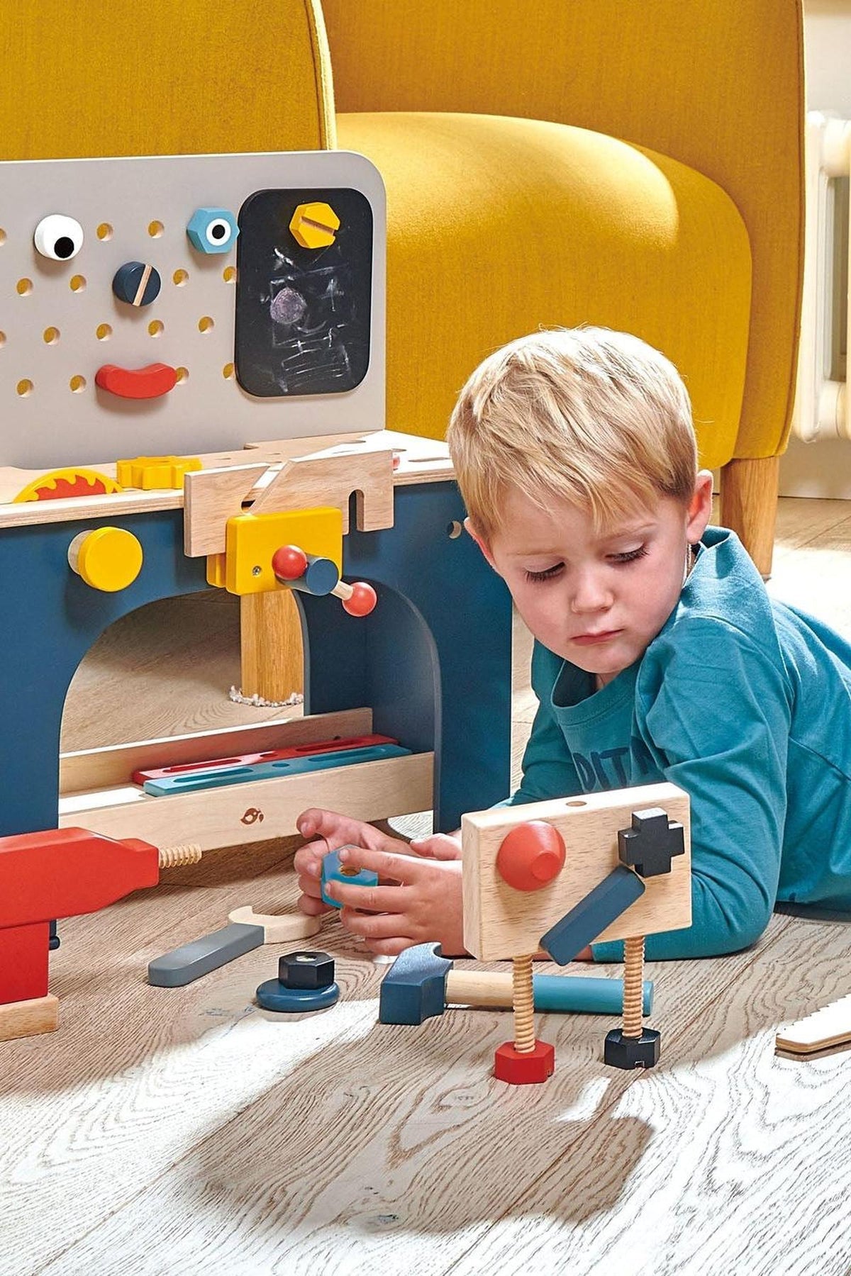 A young child plays on the floor with a colorful wooden tool bench, featuring various tools and playful design elements.