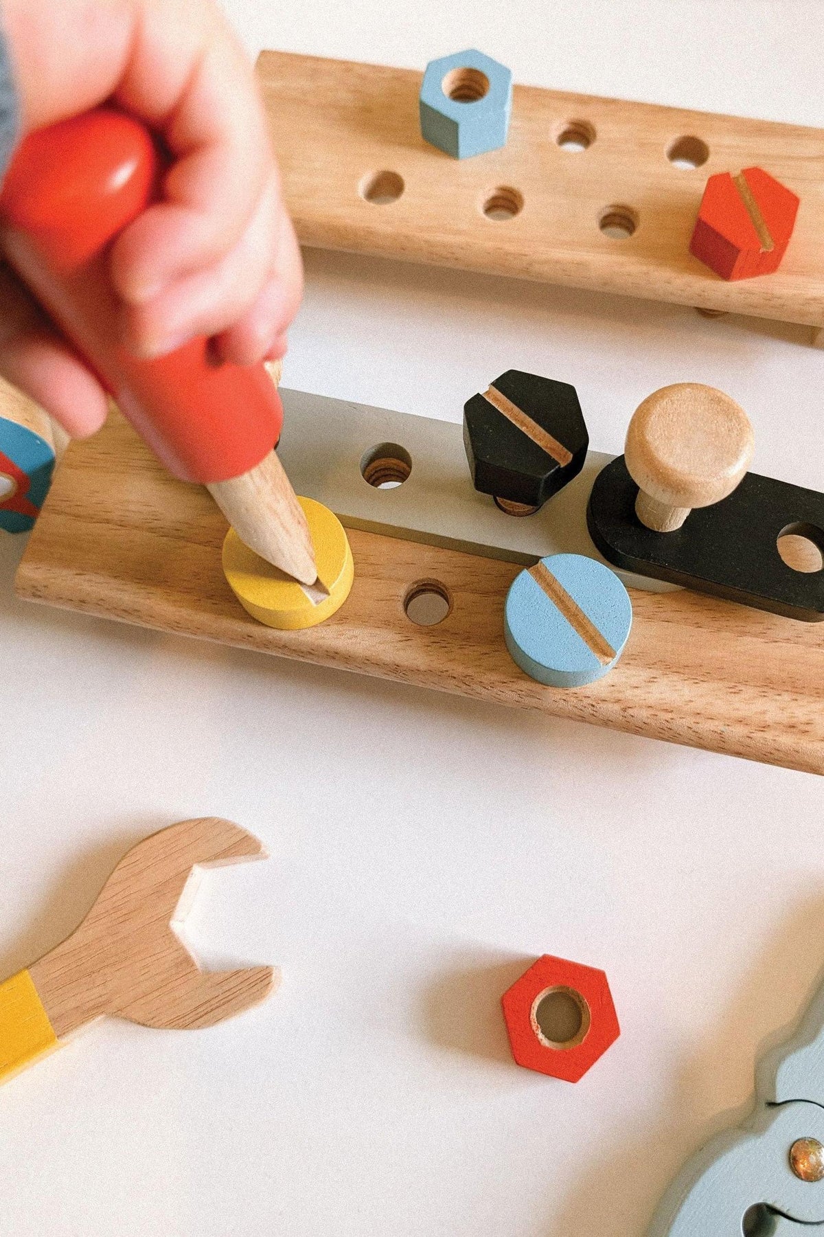 A child’s hand uses a wooden tool to press colorful shapes into a wooden base, showcasing sustainable, eco-friendly design.