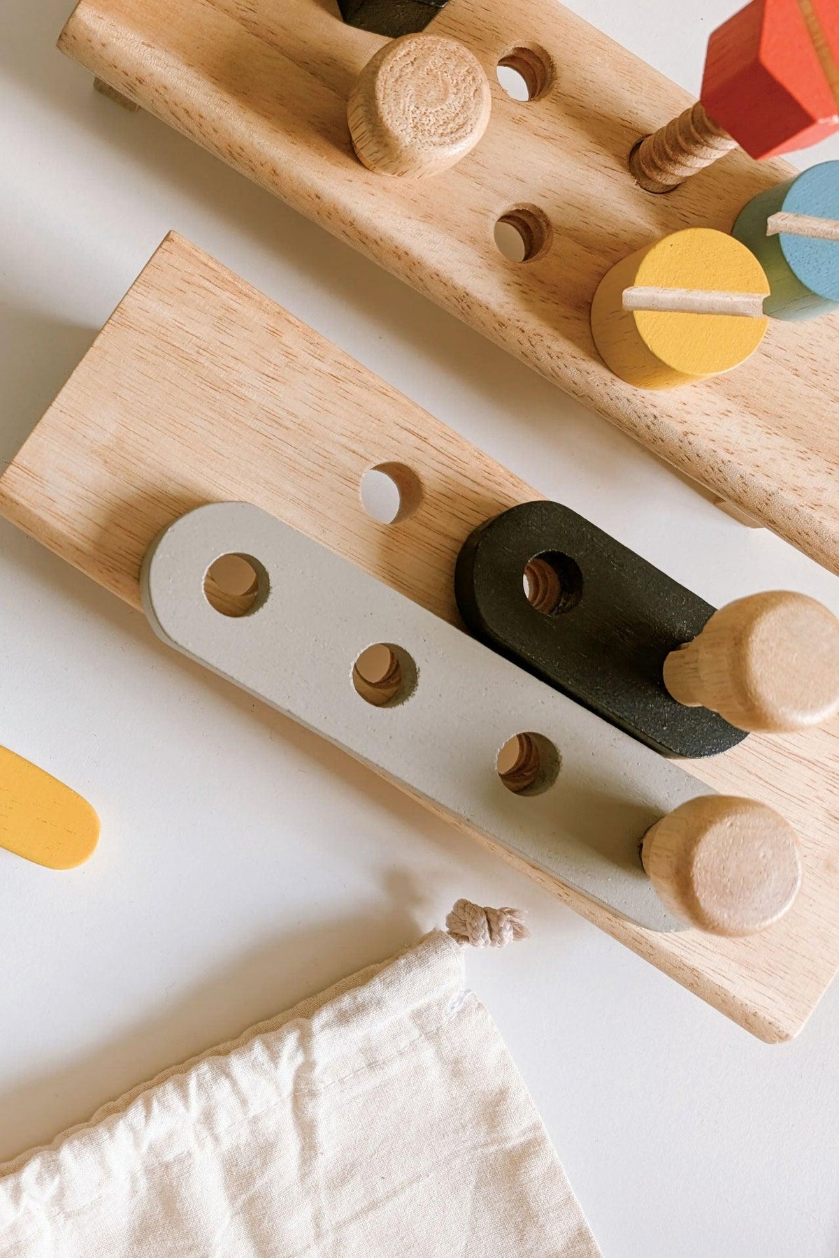 A close-up of wooden toy pieces in various colors, featuring a gray and black tool with circular cutouts and pegs.