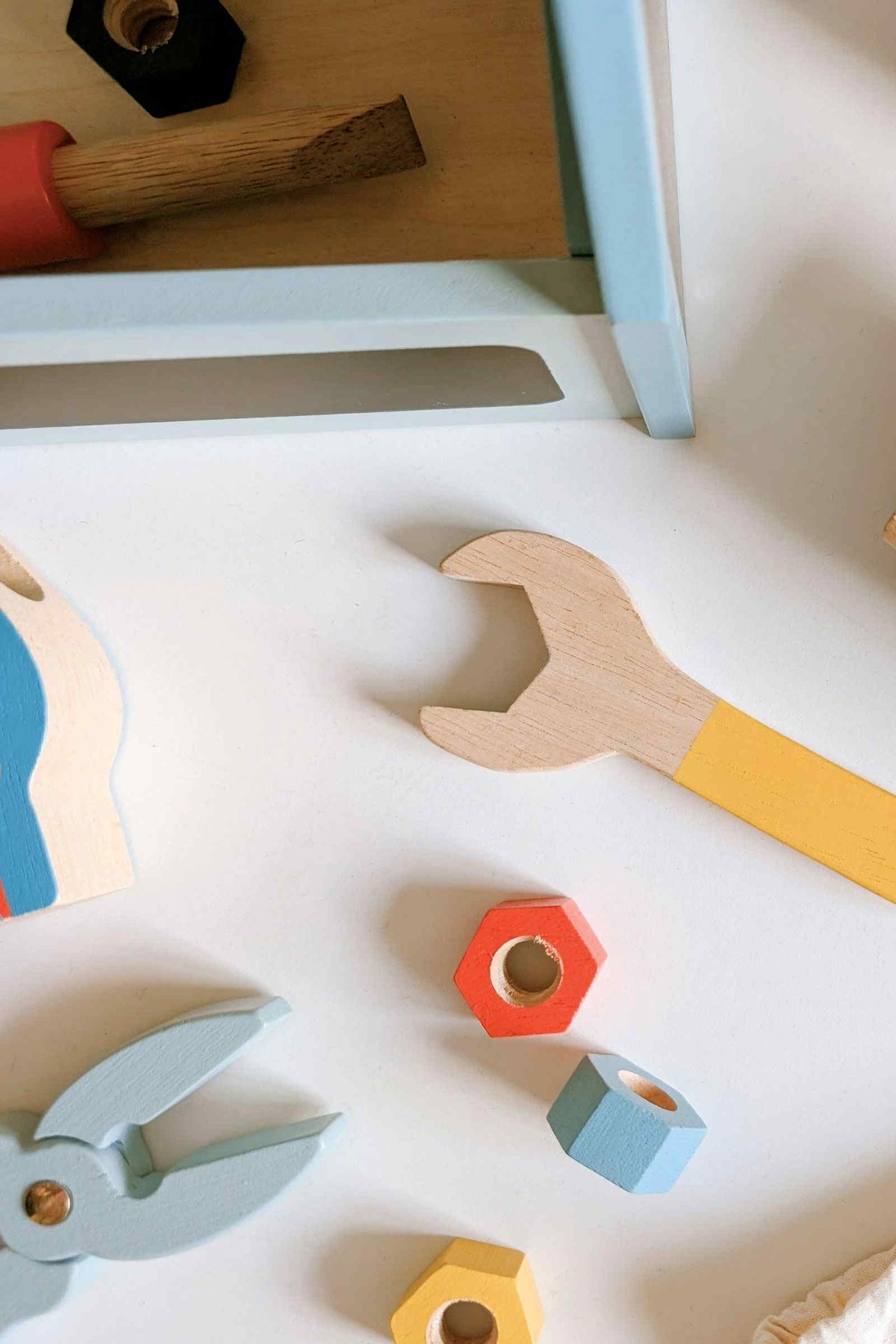 Colorful wooden tools are arranged on a light surface, featuring a yellow wrench, pliers, and various hexagonal blocks.