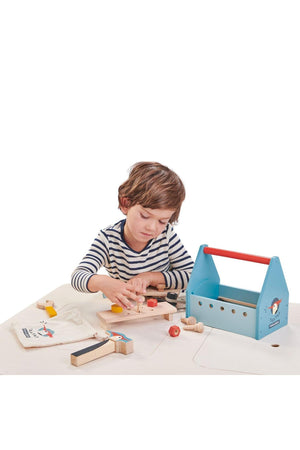 A young child engages with the Tender Leaf wooden Tap Tap Tool Box, featuring colorful wooden tools and a blue.
