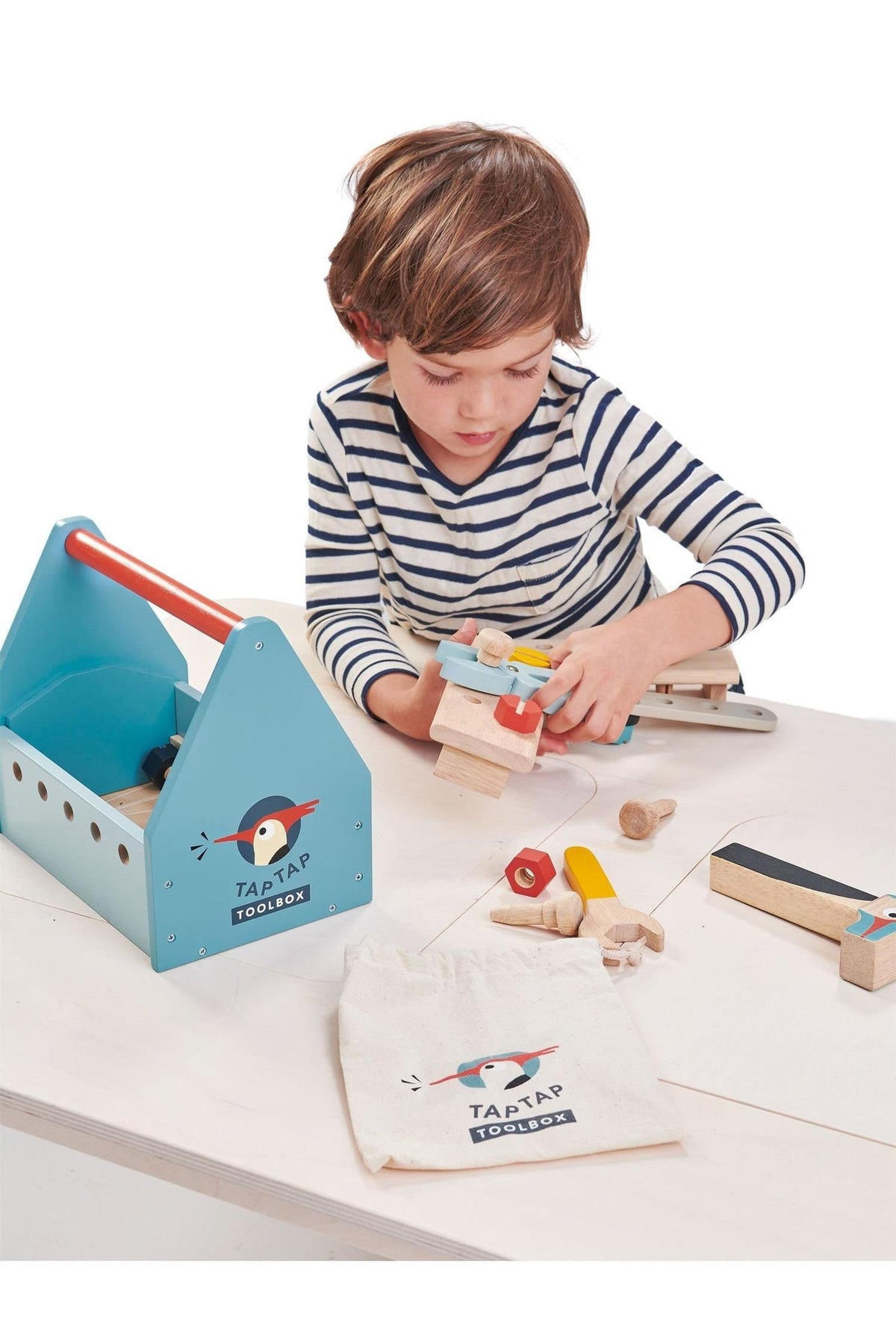 A child in a striped shirt engages with a colorful wooden toolbox, featuring various tools and a cloth storage bag.