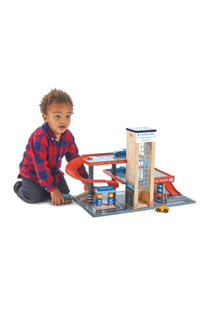 A child plays with the Tender Leaf Bluebird Service Station, featuring a wooden garage, cars, and colorful ramps.
