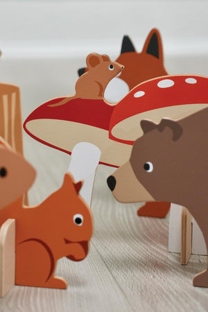 Colorful wooden animal figures, including a squirrel and bear, alongside a red toadstool, arranged on a light wooden surface.