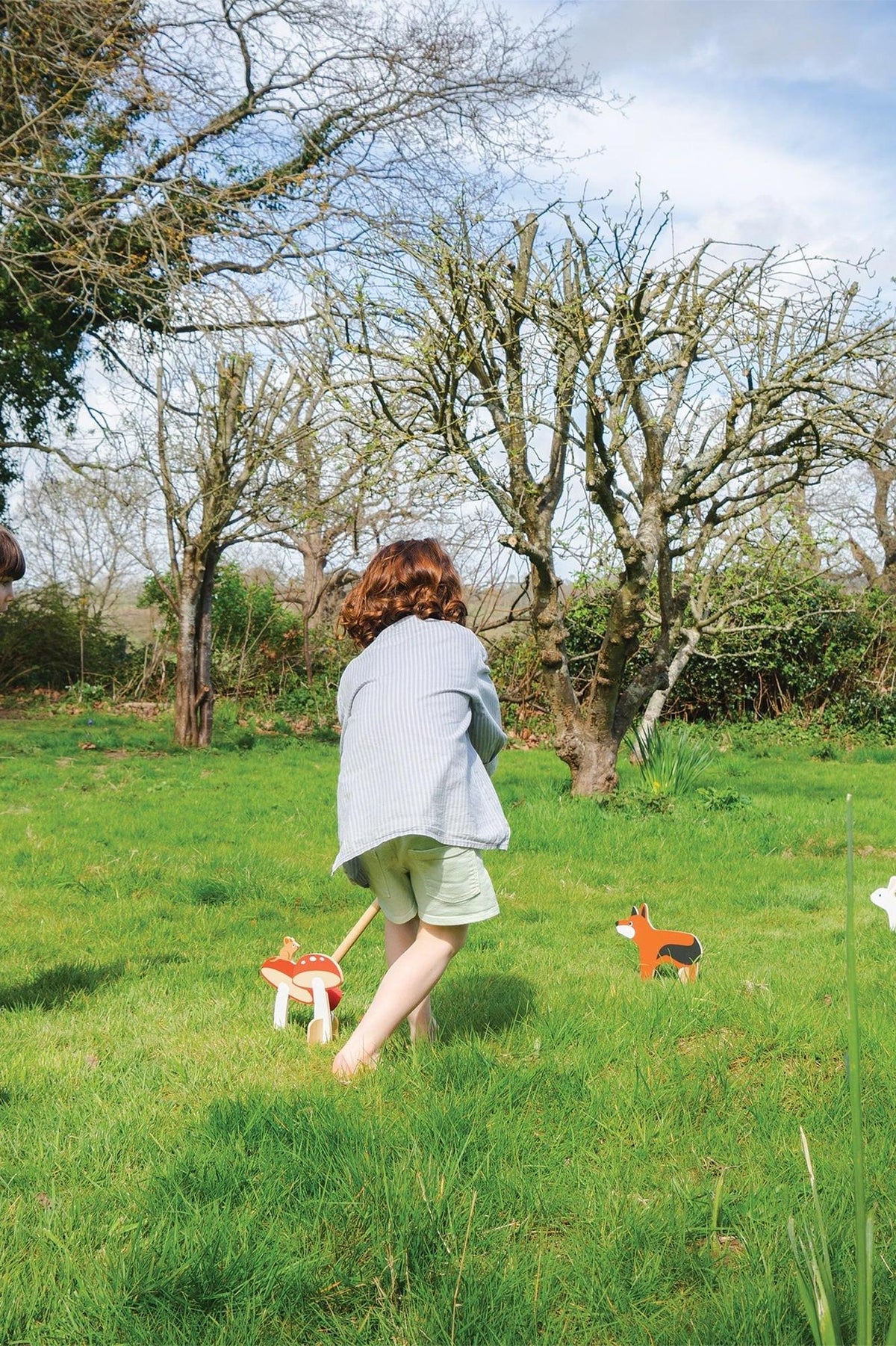 A child in a striped shirt plays croquet in a grassy yard, surrounded by wooden animal-themed croquet pieces.