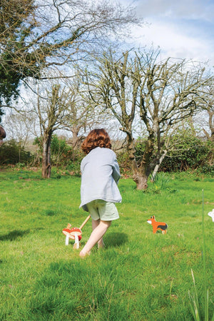 A child in a striped shirt plays croquet in a grassy yard, surrounded by wooden animal-themed croquet pieces.