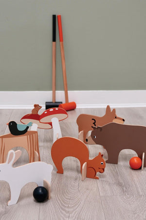 Colorful wooden croquet pieces featuring woodland animals and a toadstool, with two mallets in the background on a wooden floor.