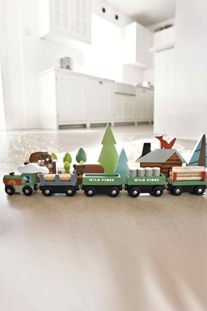 Colorful wooden train set with three carriages carrying logs, surrounded by pine trees and a cabin.