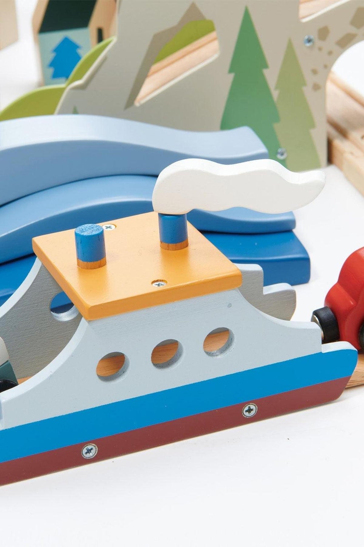 A colorful wooden toy boat features a blue hull and an orange cabin with a white smoke stack. It is part of a vibrant train set, promoting imaginative play.