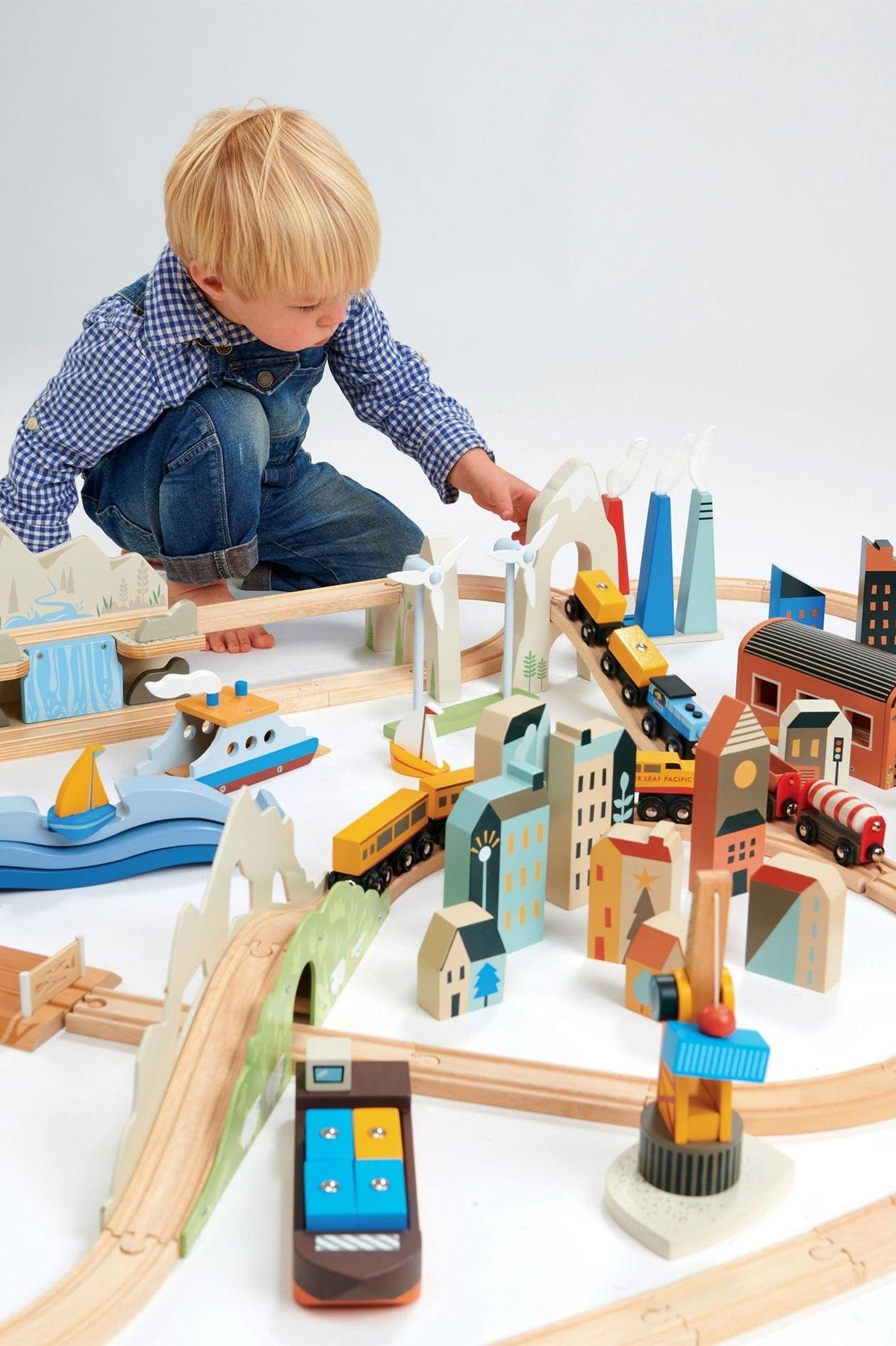 A young child plays with a colorful wooden train set featuring various buildings, vehicles, and landscapes. The eco-friendly toys encourage imaginative play and are made of sustainable materials.